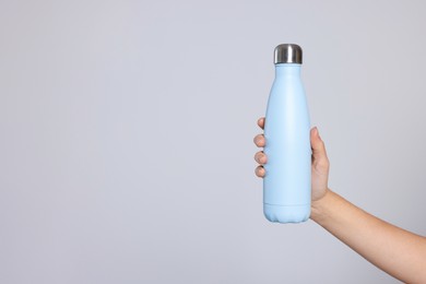 Woman holding thermo bottle on light grey background, closeup. Space for text