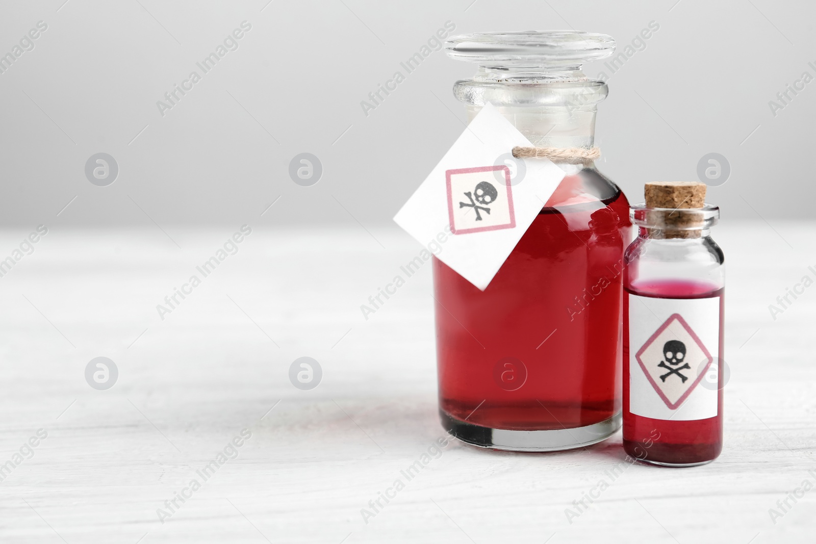 Photo of Glass bottle and vial of poison with warning signs on white wooden table. Space for text