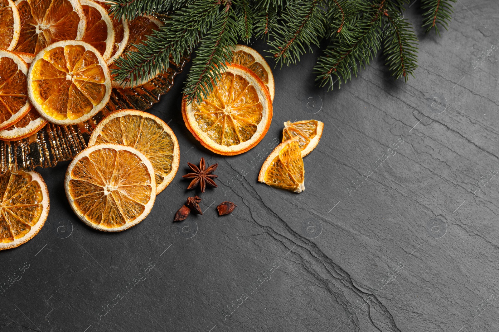 Photo of Dry orange slices, anise stars and fir tree branches on black table, flat lay. Space for text