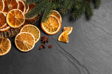 Dry orange slices, anise stars and fir tree branches on black table, flat lay. Space for text