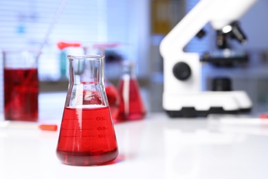 Photo of Laboratory analysis. Glass flask with red liquid and microscope on white table indoors, space for text