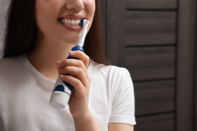 Photo of Woman brushing her teeth with electric toothbrush in bathroom, closeup