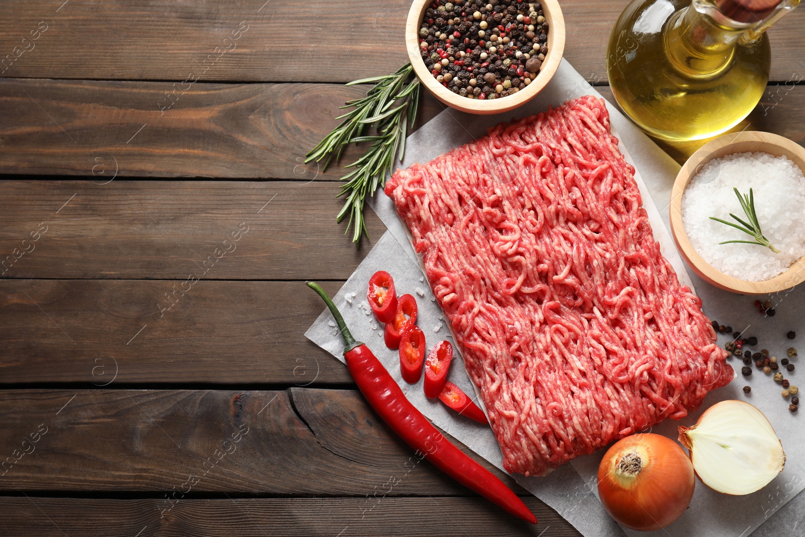 Photo of Raw ground meat, spices, rosemary, oil and onion on wooden table, flat lay. Space for text