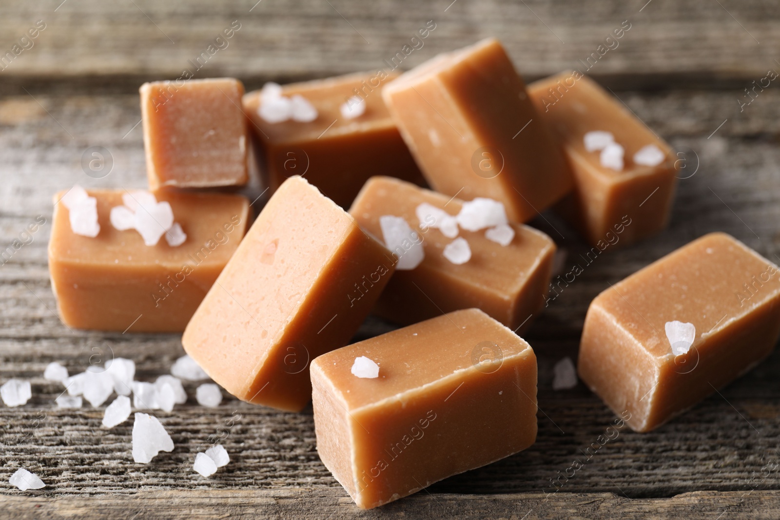 Photo of Yummy caramel candies with sea salt on wooden table, closeup