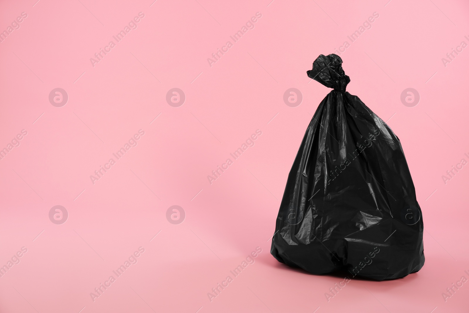Photo of Trash bag full of garbage on pink background. Space for text