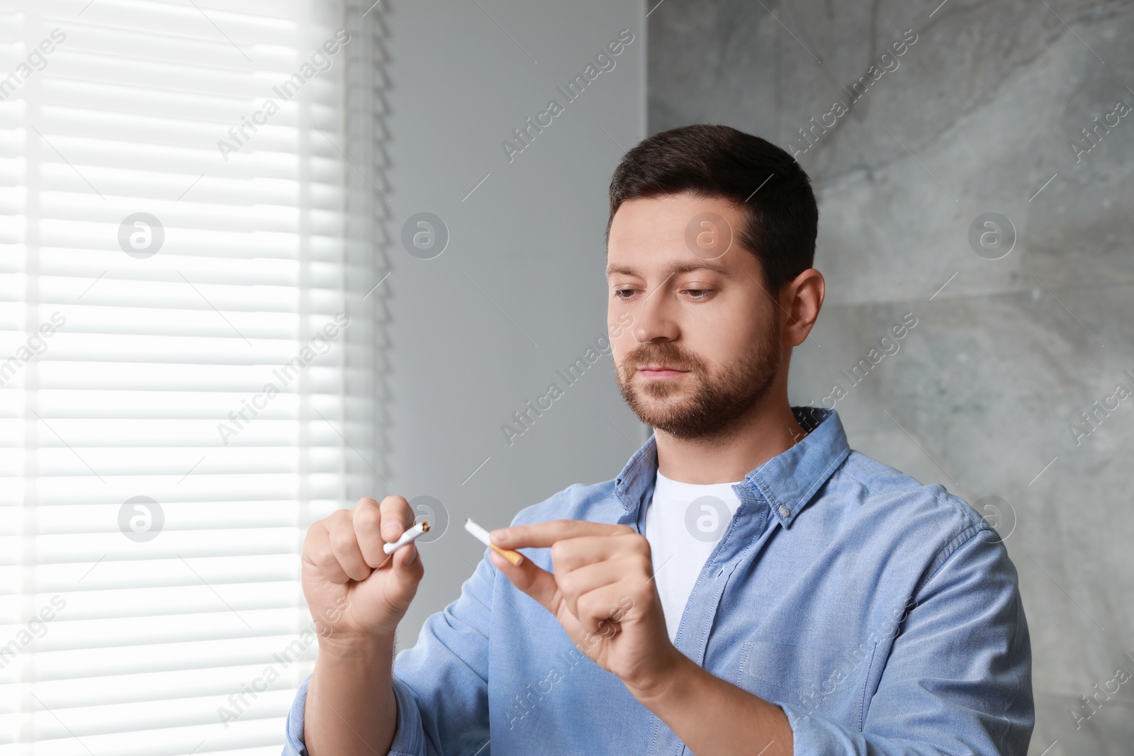 Photo of Stop smoking concept. Man holding pieces of broken cigarette indoors