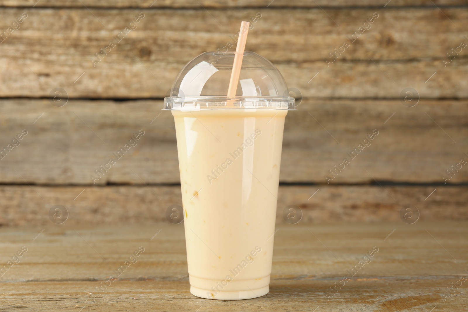 Photo of Plastic cup of tasty smoothie on wooden table