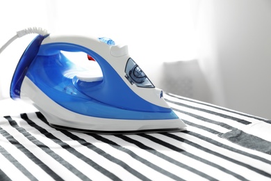 Photo of Modern electric iron on board indoors, space for text. Household appliance