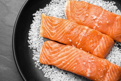 Photo of Fresh raw salmon with salt on black table, top view