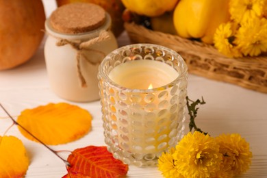 Burning candle, chrysanthemums and yellow leaves on white wooden table