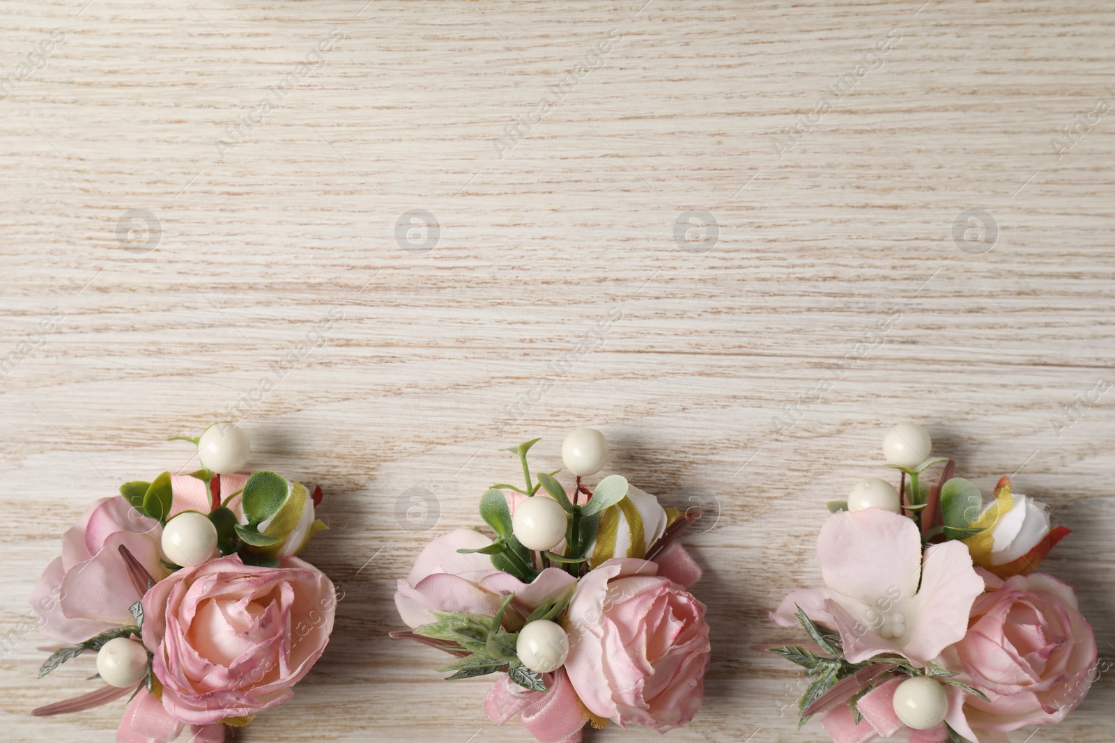 Photo of Stylish pink boutonnieres on white wooden table, flat lay. Space for text