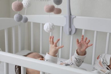 Cute little baby lying in crib with hanging mobile