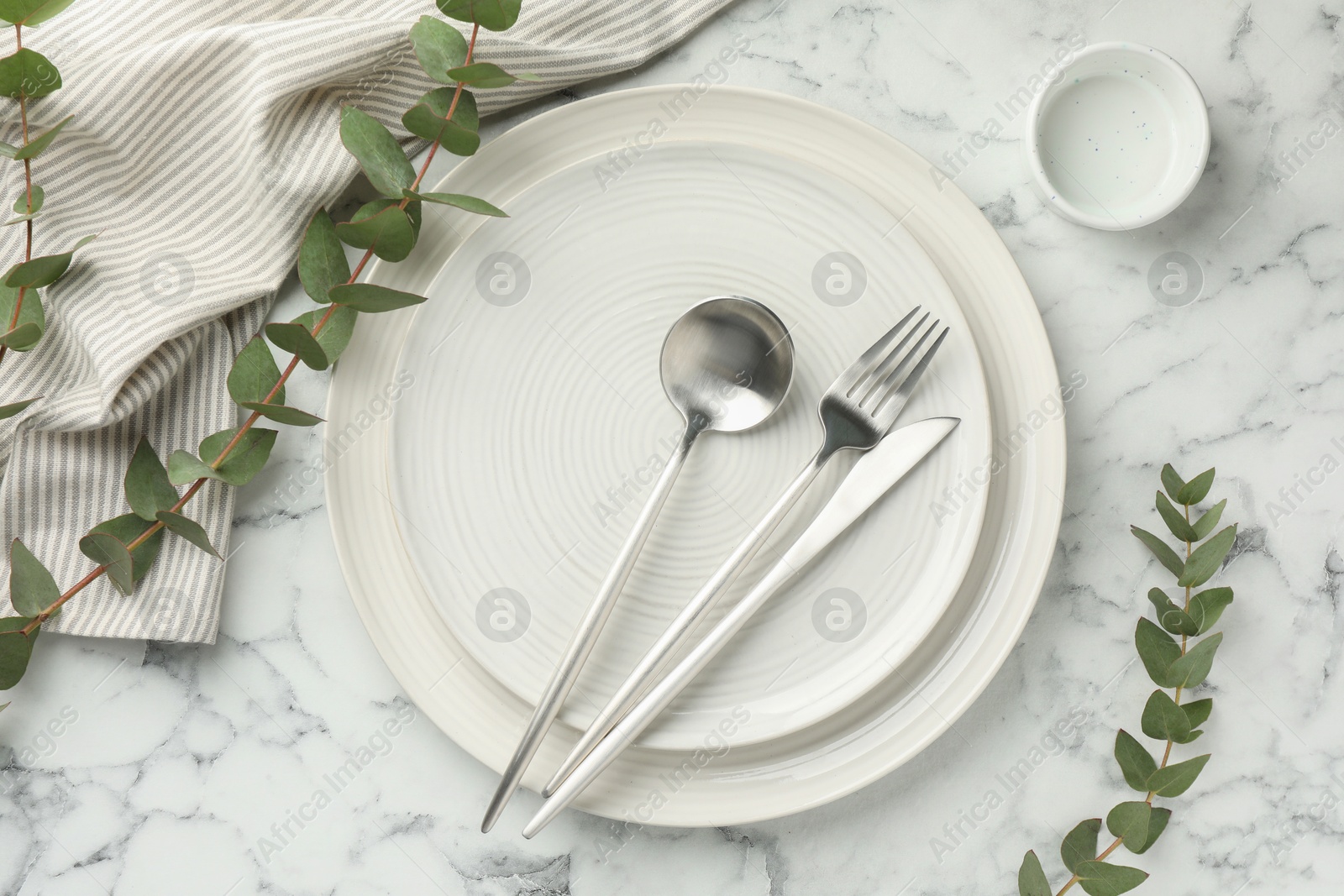 Photo of Stylish setting with cutlery, napkin, eucalyptus branches and plates on white marble table, flat lay