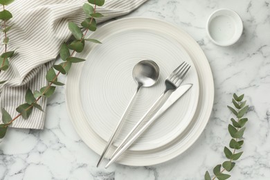 Photo of Stylish setting with cutlery, napkin, eucalyptus branches and plates on white marble table, flat lay