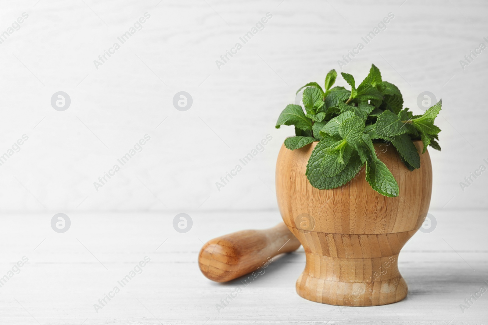 Photo of Wooden mortar with fresh green mint and pestle on table. Space for text