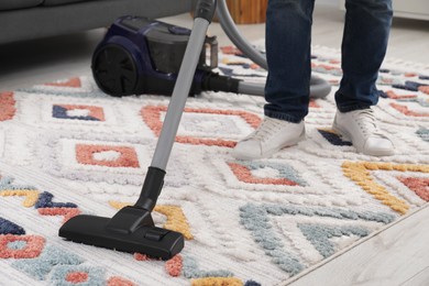 Photo of Man cleaning carpet with vacuum cleaner at home, closeup