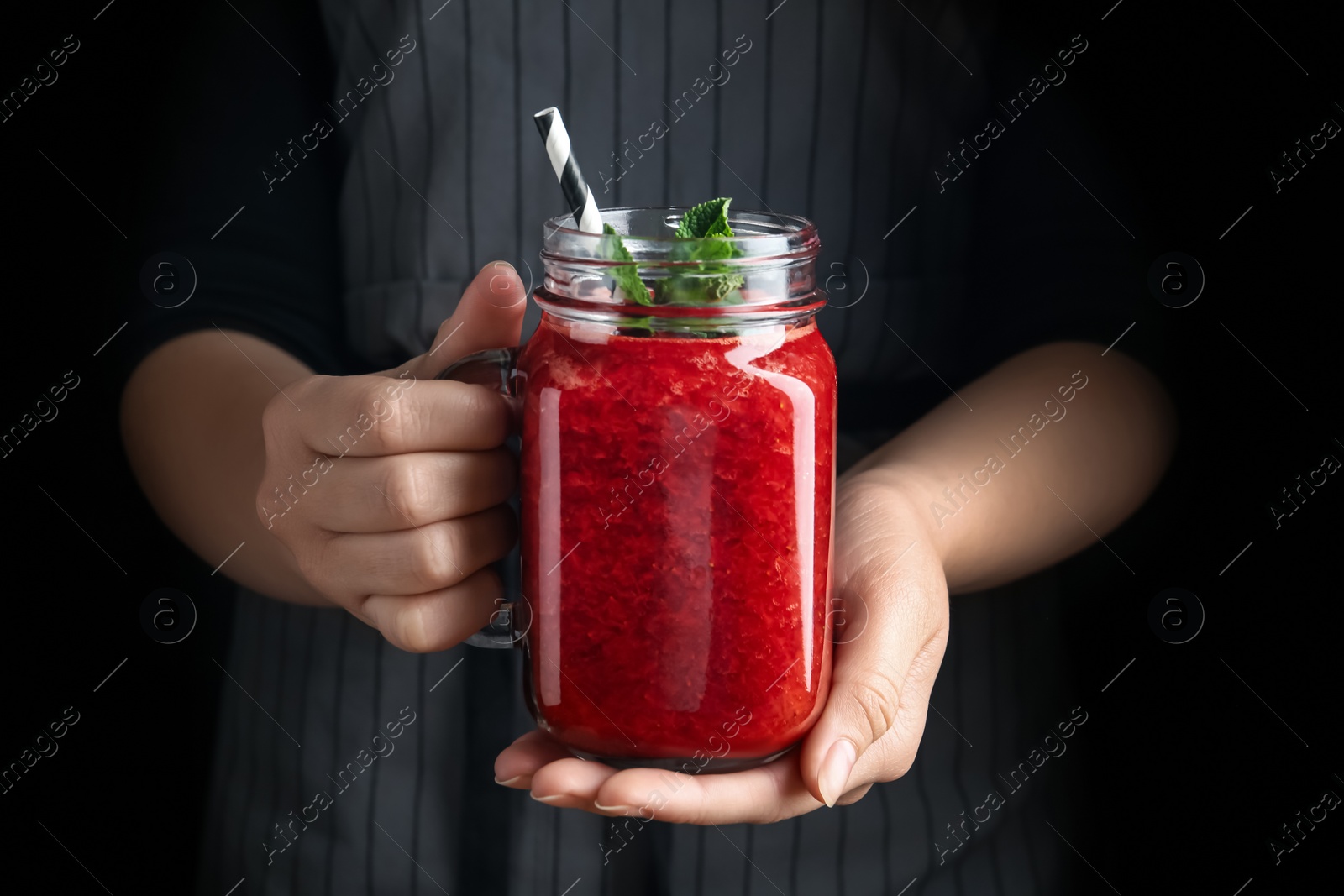 Photo of Woman holding tasty strawberry smoothie with mint on black background, closeup