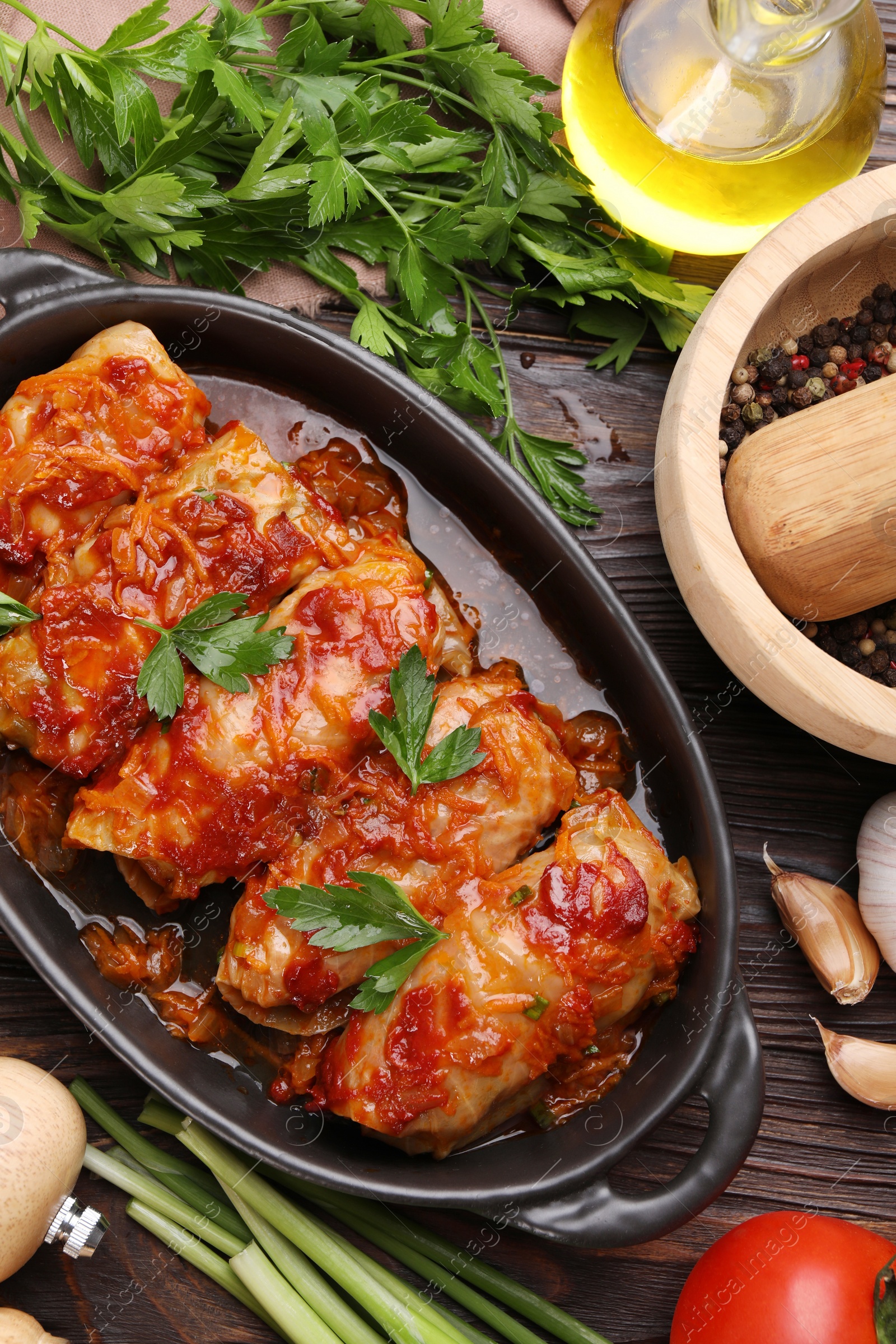 Photo of Delicious stuffed cabbage rolls cooked with tomato sauce and ingredients on wooden table, flat lay