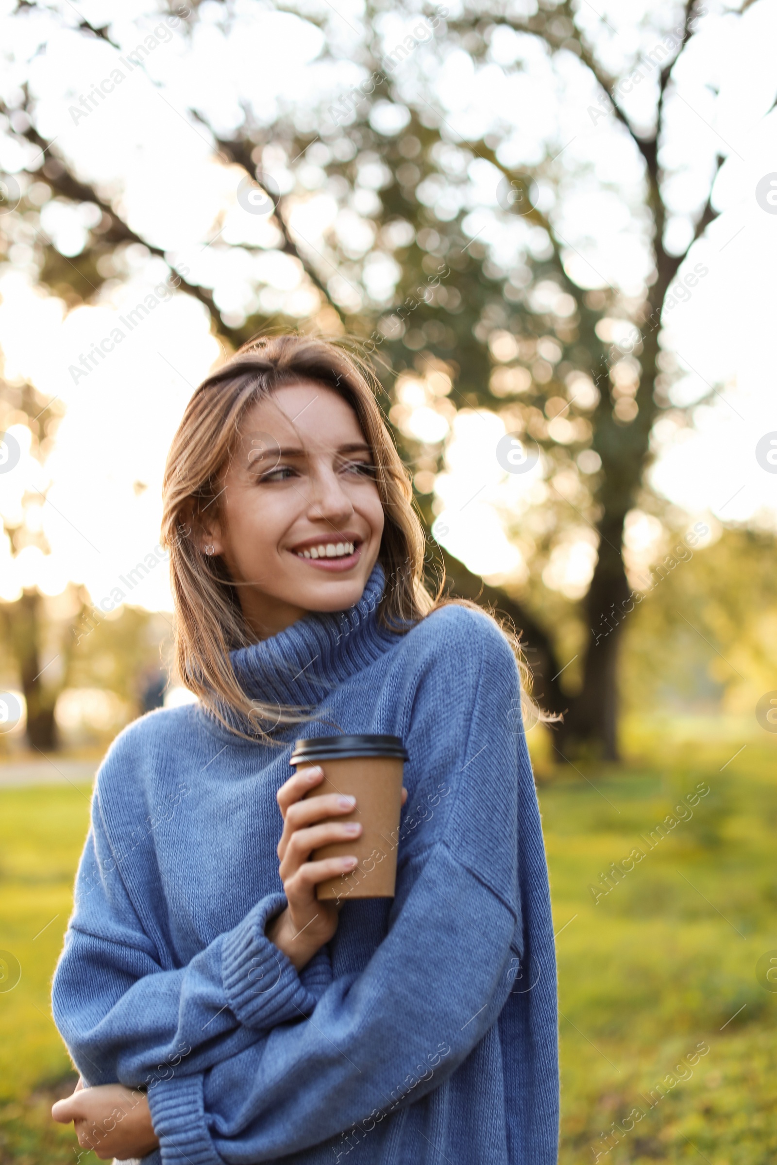 Photo of Beautiful young woman with coffee cup wearing stylish sweater in autumn park