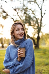 Beautiful young woman with coffee cup wearing stylish sweater in autumn park