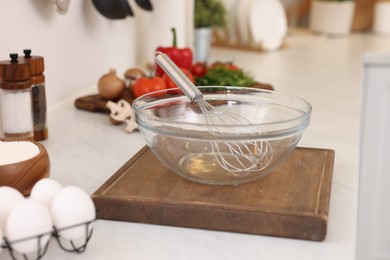 Photo of Metal whisk, bowl and different products on light table in kitchen