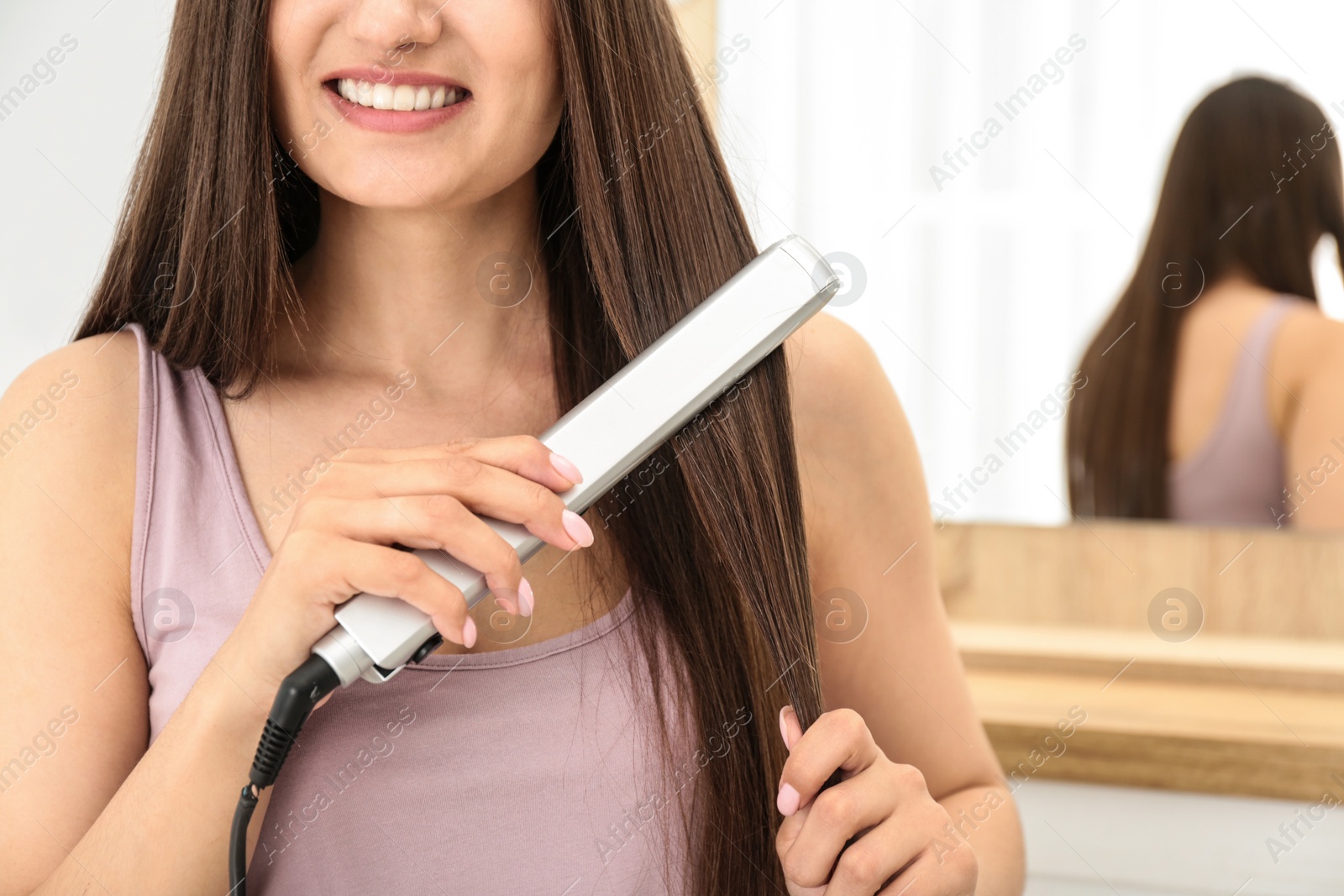 Photo of Young woman using hair iron indoors, closeup. Space for text