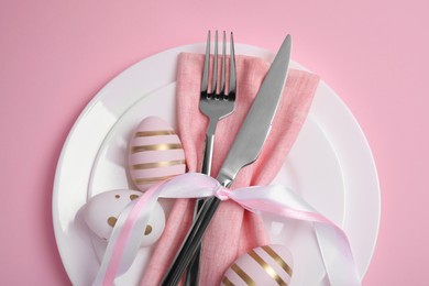 Photo of Festive table setting with painted eggs and cutlery on pink background, above view. Easter celebration