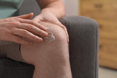 Photo of Man applying ointment onto his knee indoors, closeup. Space for text