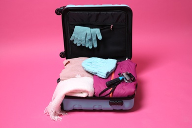 Photo of Open suitcase with warm clothes and action camera on color background. Winter vacation