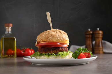 Photo of Plate with delicious vegetarian burger on grey textured table