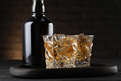 Photo of Whiskey with ice cubes in glasses and bottle on black wooden table, closeup