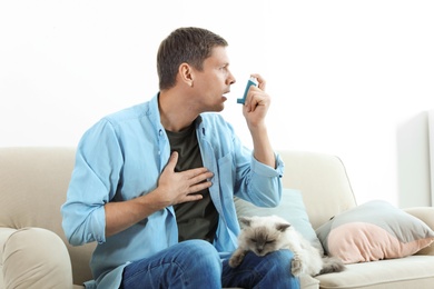 Photo of Man using asthma inhaler near cat at home. Health care