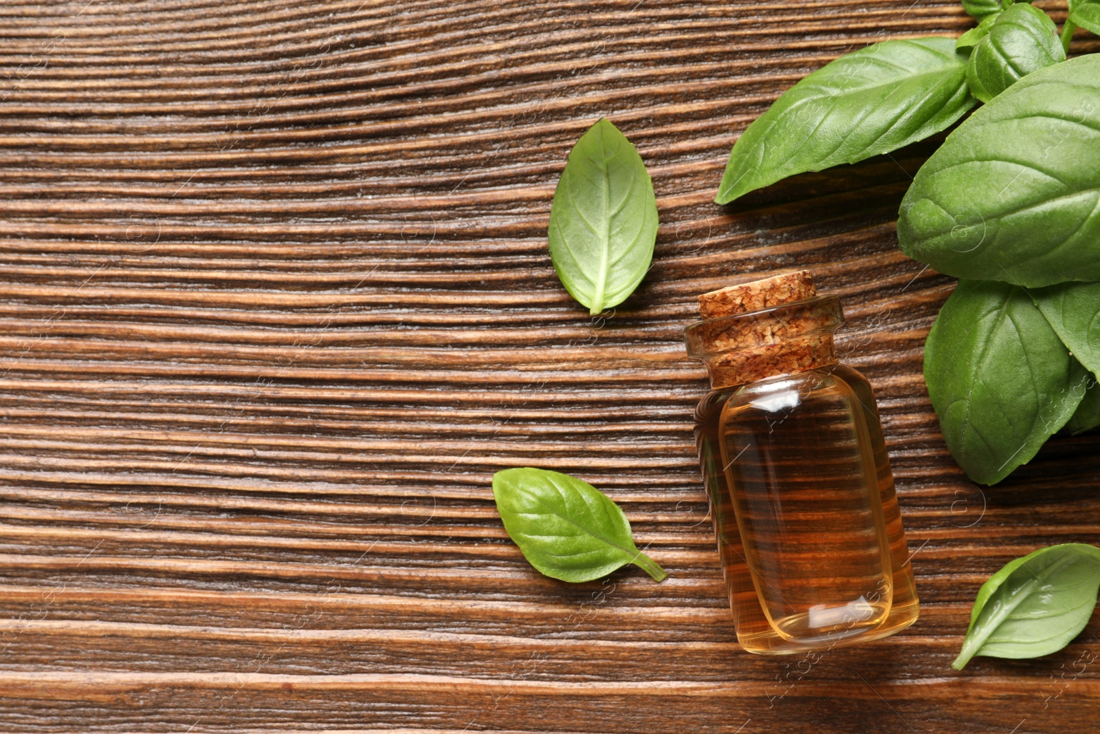 Photo of Glass bottle of basil essential oil and leaves on wooden table, flat lay. Space for text