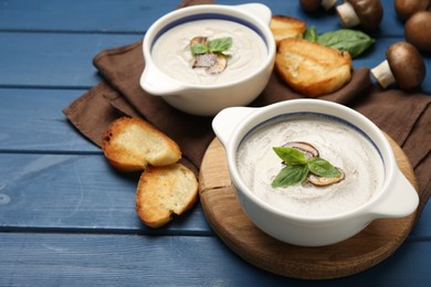 Photo of Delicious mushroom soup in ceramic pots and fresh ingredients on blue wooden table. Space for text