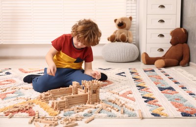 Photo of Little boy playing with wooden construction set on carpet in room, space for text. Child's toy