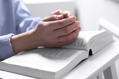 Photo of Religion. Christian woman praying over Bible indoors, closeup