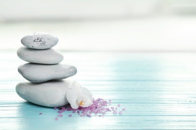 Photo of Spa stones, sea salt and flower on table against blurred background. Space for text