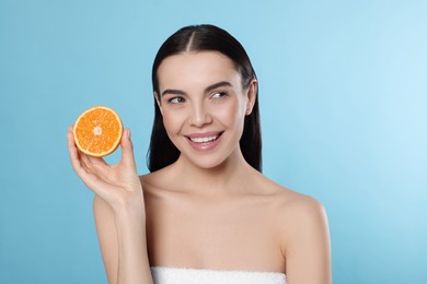 Photo of Woman holding half of orange on light blue background. Spa treatment