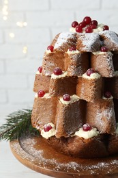 Photo of Delicious Pandoro Christmas tree cake with powdered sugar and berries on white table near brick wall, closeup