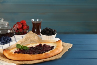 Photo of Delicious sweet cottage cheese pastry with cherry jam and fresh berries on blue wooden table. Space for text