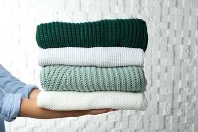 Photo of Woman holding stack of warm clothes on white background, closeup. Autumn season