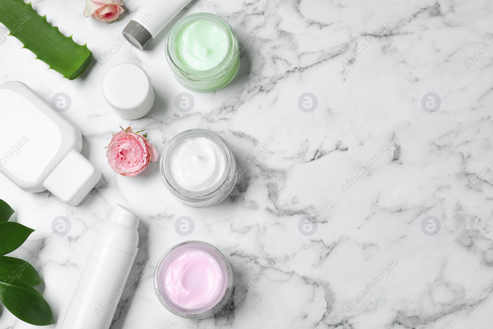 Photo of Flat lay composition with jars of organic cream and flowers on white marble table. Space for text