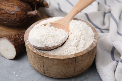 Photo of Wooden bowl and spoon with cassava flour on grey table, closeup