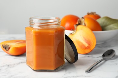 Photo of Delicious persimmon jam and fresh fruits on white marble table
