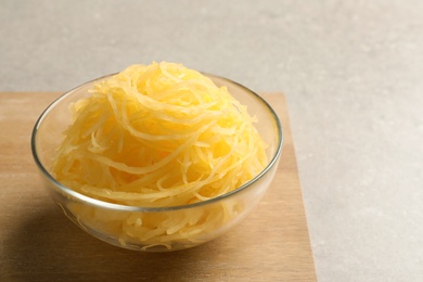 Photo of Bowl with cooked spaghetti squash on wooden board