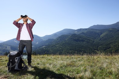 Photo of Tourist with hiking equipment looking through binoculars in mountains