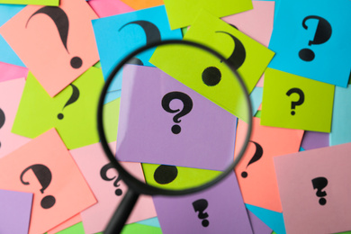 Photo of Magnifier glass above different colorful paper cards with question marks, top view