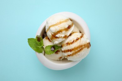 Photo of Scoops of tasty ice cream with mint leaves and caramel sauce on light blue background, top view