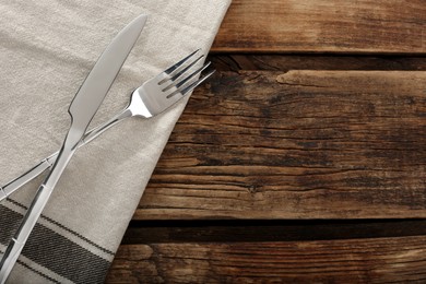 Photo of Fork, knife and napkin on wooden table, top view with space for text. Stylish shiny cutlery set