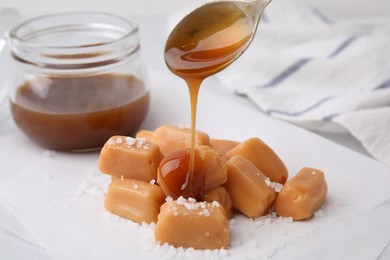 Photo of Pouring delicious salted caramel on candies on white table
